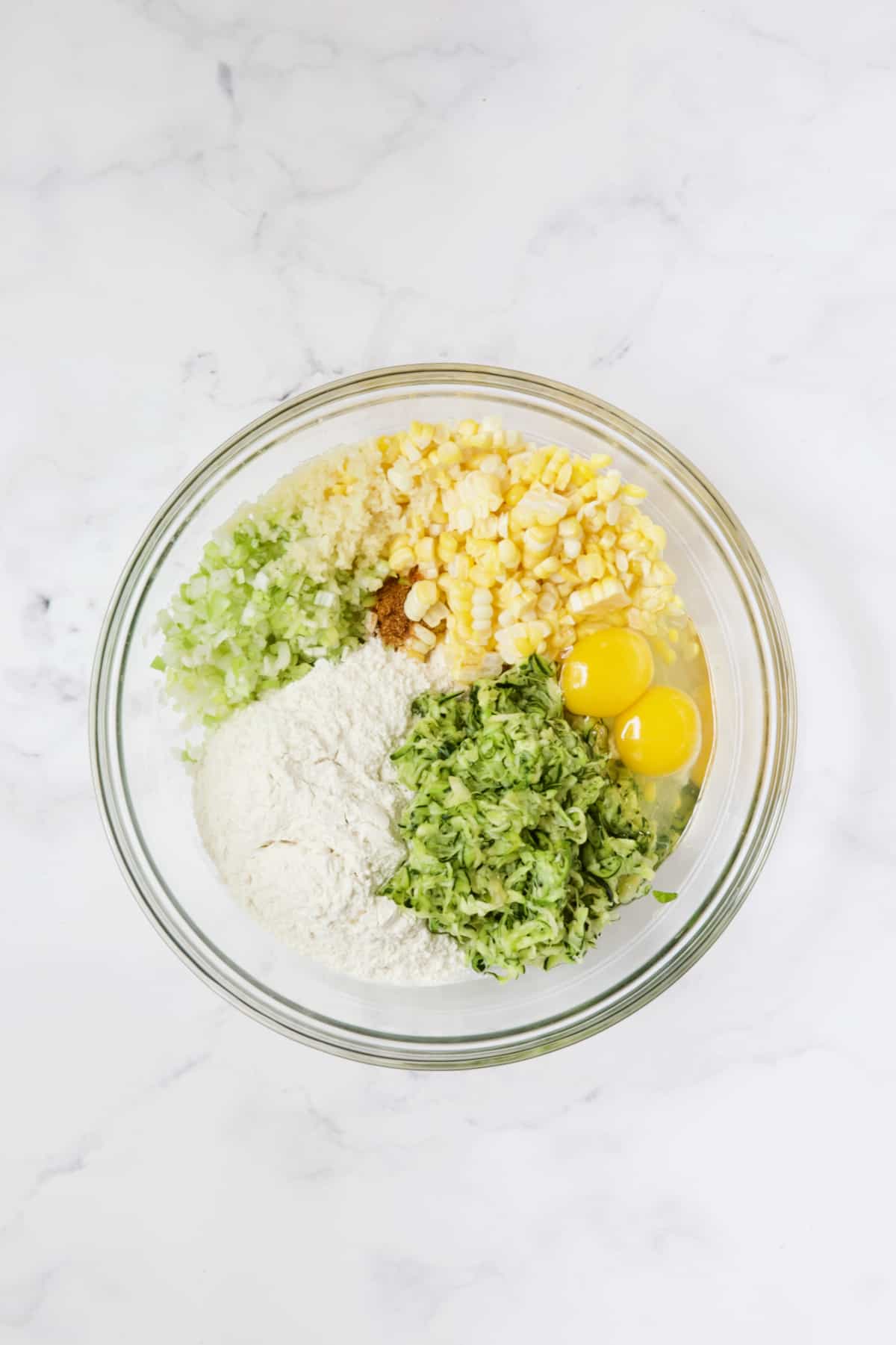 Ingredients for Zucchini Corn Fritters in glass bowl not yet blended together.