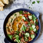 Loaded Roasted Eggplant Dip (Baba Ganoush) in blue dish with pita wedges and pine nuts.
