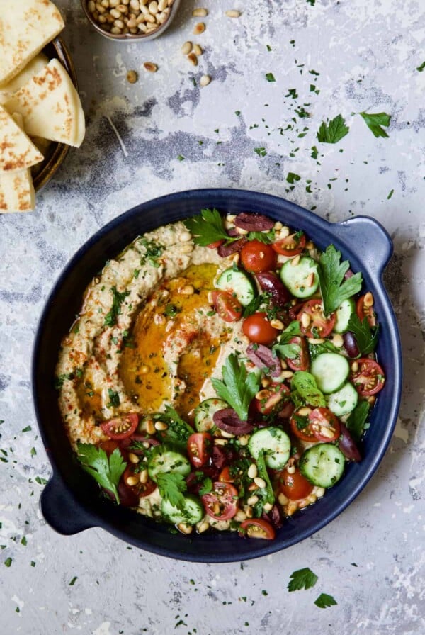 Loaded Roasted Eggplant Dip (Baba Ganoush) in blue dish with pita wedges and pine nuts.