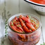 Tomato Confit in glass jar garnished with fresh thyme.