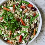 Mediterranean Barley Salad with Green Beans, Red Bell Pepper, Olives and Feta in serving bowl with serving spoon garnished with fresh parsley.