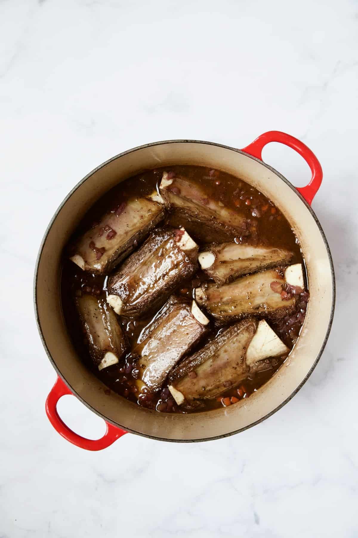 Beef short ribs after being browned then placed in red wine in red enamel Dutch oven.