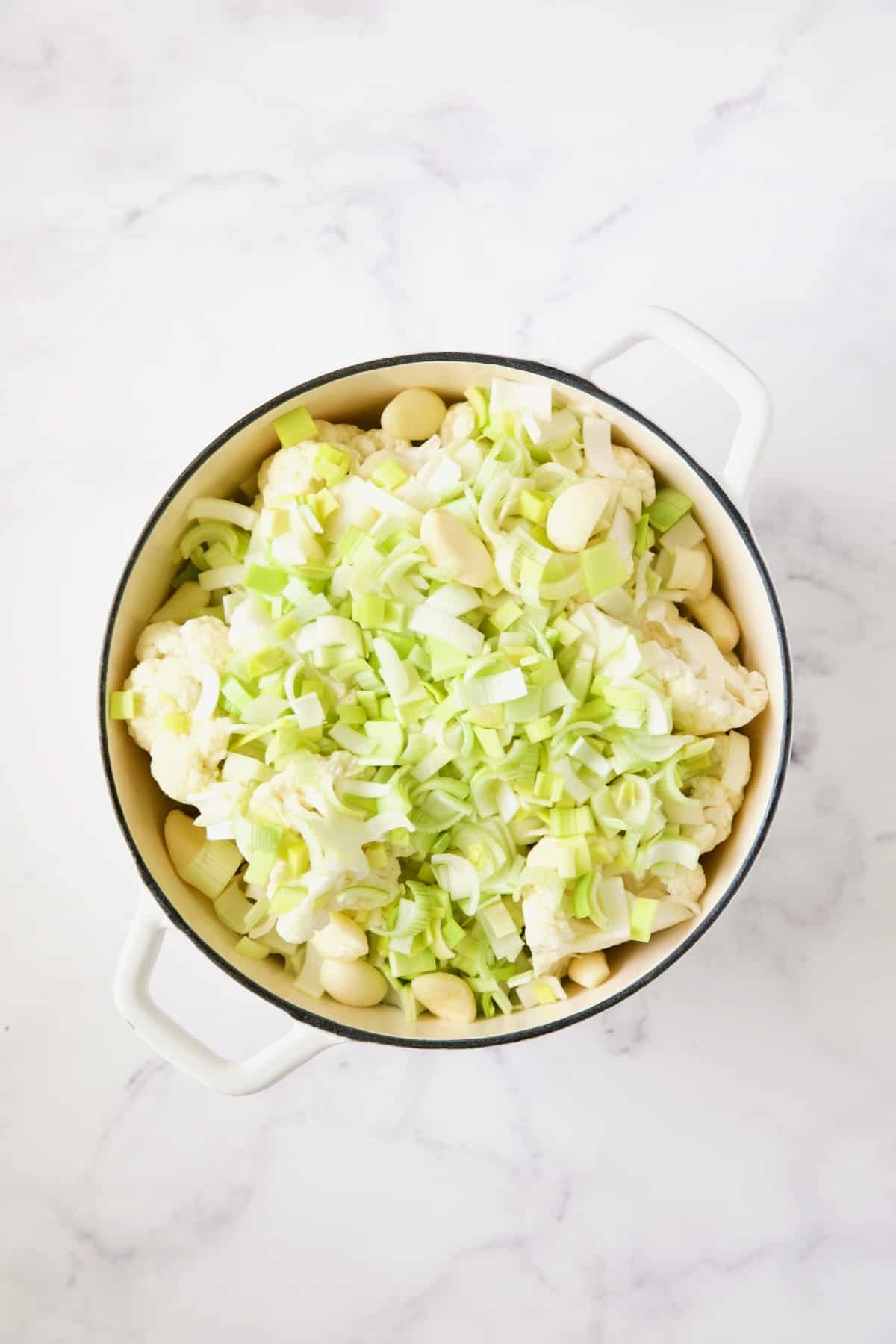 Cauliflower, leeks, garlic and chicken broth in white enamel Dutch oven.