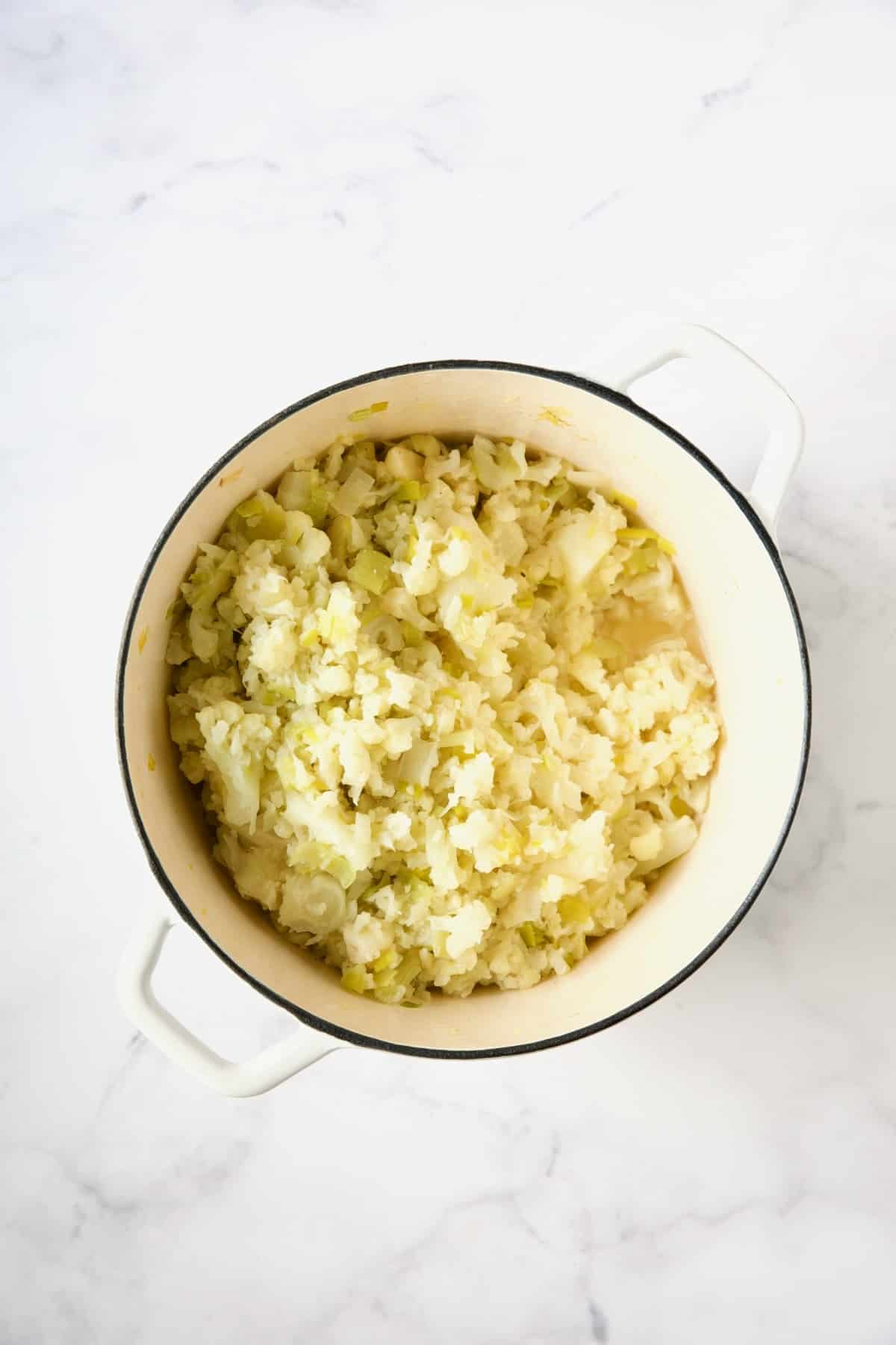 Cauliflower, leeks, garlic and chicken broth in white enamel Dutch oven after being cooked.