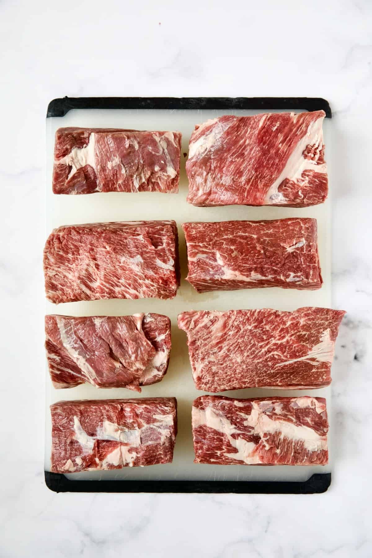 Eight short ribs on white plastic cutting board.
