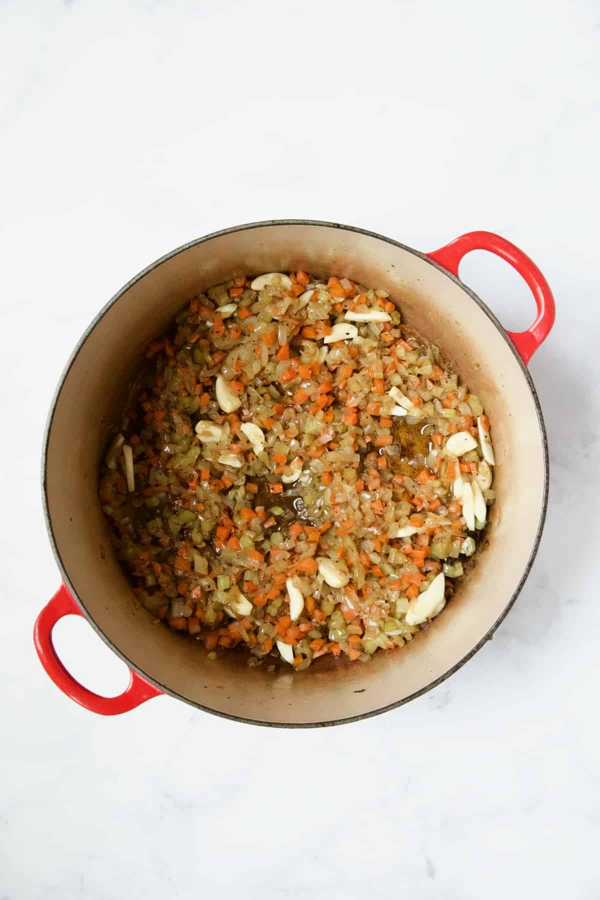 Cooked onions, celery, carrots and garlic in red enamel Dutch oven.