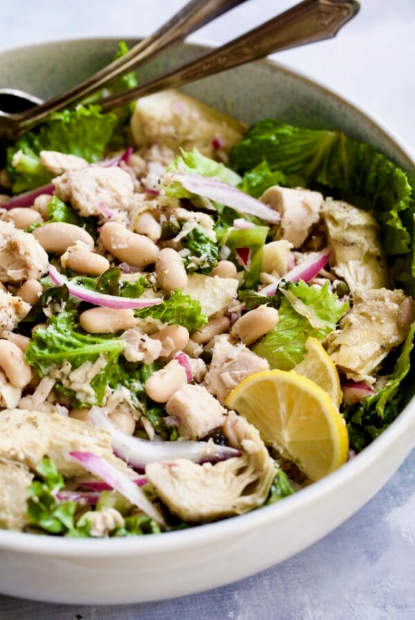 Finished salad in white serving bowl with silver serving utensils.