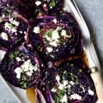 Roasted Red Cabbage Steaks with Balsamic Vinaigrette and Goat Cheese on white platter with serving fork.