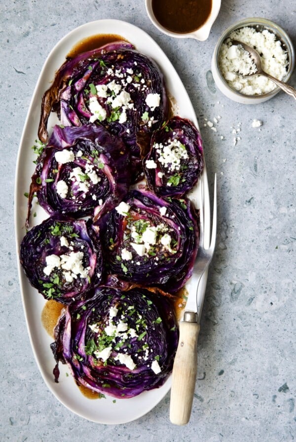 Roasted Red Cabbage Steaks with Balsamic Vinaigrette and Goat Cheese on white oval platter on pale blue background.