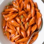 Bourbon-Glazed Carrots with Honey in white serving bowl with fresh thyme.