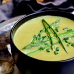Cream of Asparagus and Leek Soup with Curry in black bowl garnished with chives.