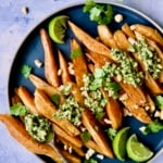 Roasted Sweet Potato Wedges with Cilantro - Cashew Sauce on round plate with cilantro and lime wedges.