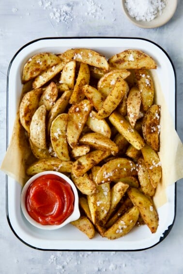 Perfect Roasted Potato Wedges in white enamel tray with ketchup and coarse sea salt.