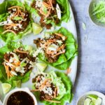 Assembled Beef Lettuce Wraps Recipe with Lime Ginger Dipping Sauce with lime wedges on gray platter.