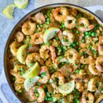 Brown Rice Paella with Shrimp and Chorizo in white enamel cast iron skillet on wood cutting board.