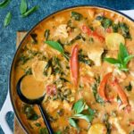 Vegan Thai Red Curry in white enamel cast iron skillet with black serving spoon.