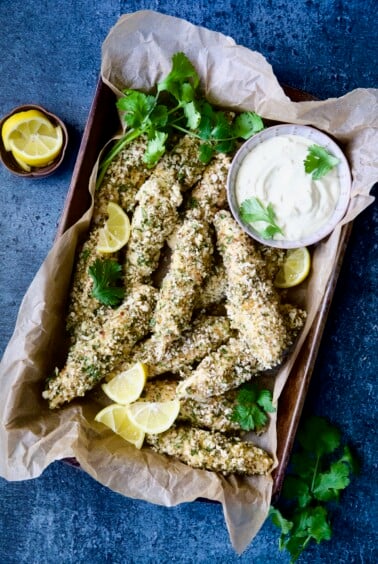 Almond Chicken Tenders with Lemon Curry Mayonnaise in parchment paper-lined pan garnished with lemon wedges and cilantro.