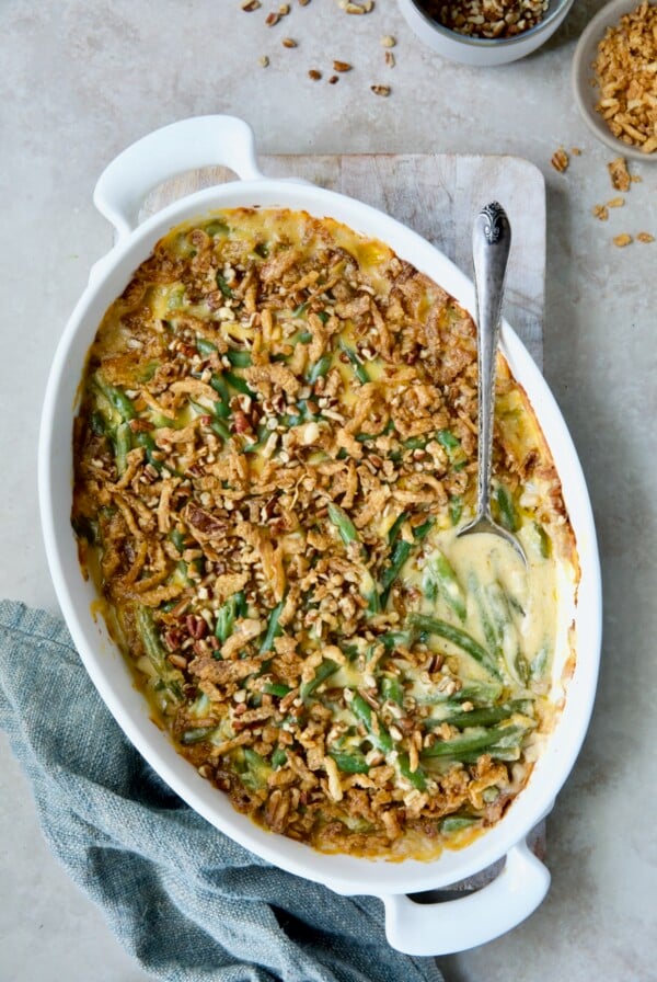 Cheesy Green Bean Casserole in white oval gratin dish with serving spoon and blue napkin.