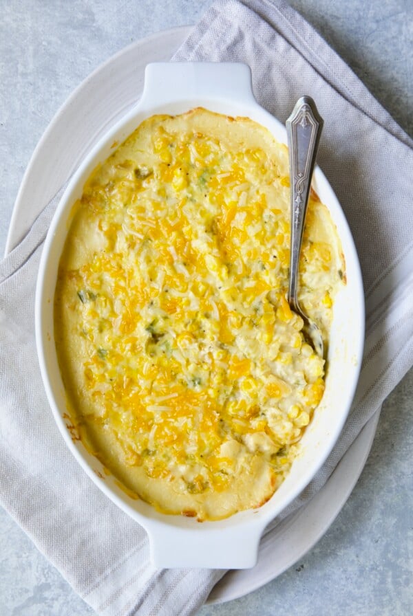 Cream Cheese Corn Casserole with Green Chiles in white oval baking dish with serving spoon.