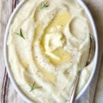 Creamy Turnip Potato Puree in white oval bowl with serving spoon on napkin with red stripe.