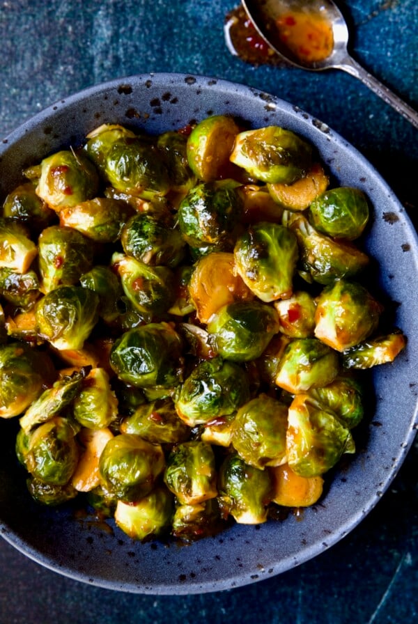 Sriracha Sweet Chili Roasted Brussels Sprouts in gray speckled bowl with spoon above it.