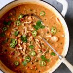 Spicy Chicken, Sweet Potato and Peanut Soup garnished with cilantro and jalapeno slices in white Dutch oven.