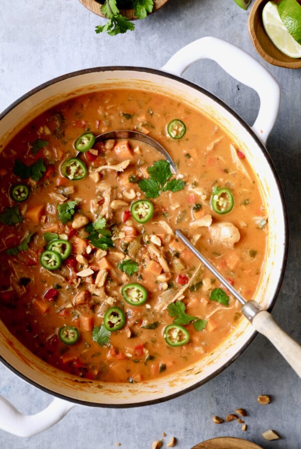 Spicy Chicken, Sweet Potato and Peanut Soup garnished with cilantro and jalapeno slices in white Dutch oven.