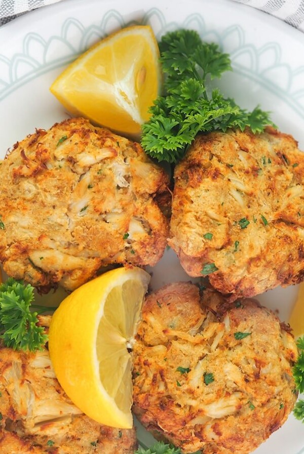 Four Air Fryer Crab Cakes on white plate garnished with parsley and lemons.