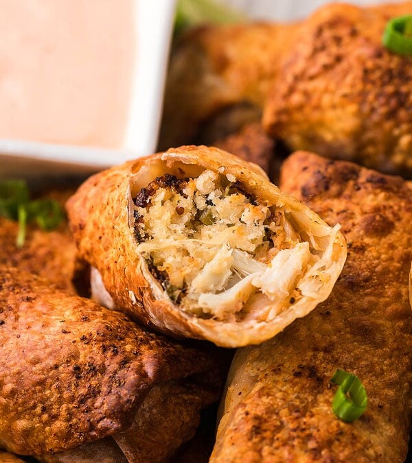 Air Fryer Crab Cake Egg Rolls cut to expose filling with dipping sauce in the background.