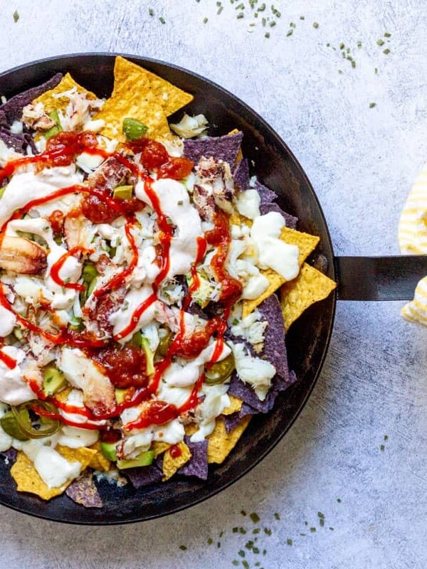 Crab Nachos in skillet with yellow striped towel on blue background.