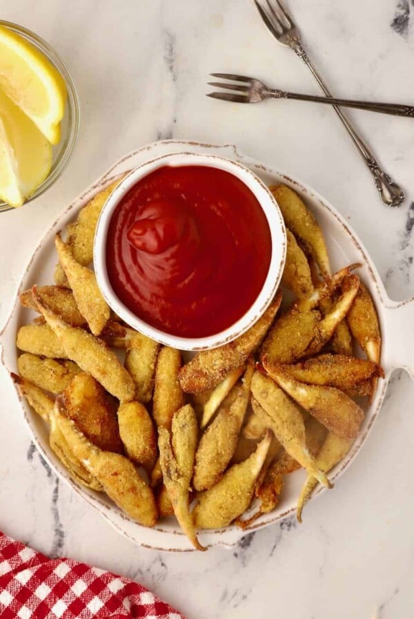 Fried Crab Claws with cocktail dipping sauce on white fish-shaped plate.