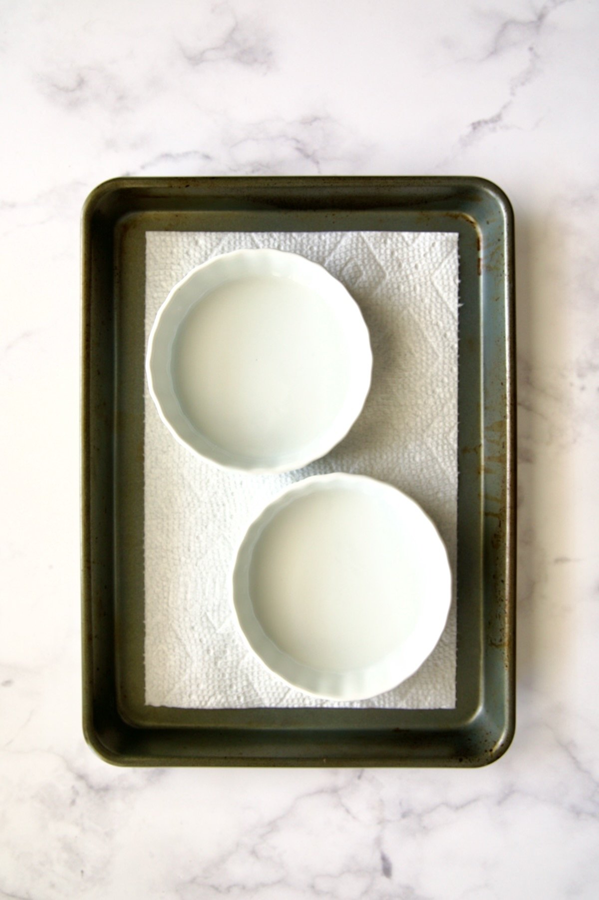 Two empty creme brulee dishes on dry paper towel set in rimmed sheet pan.