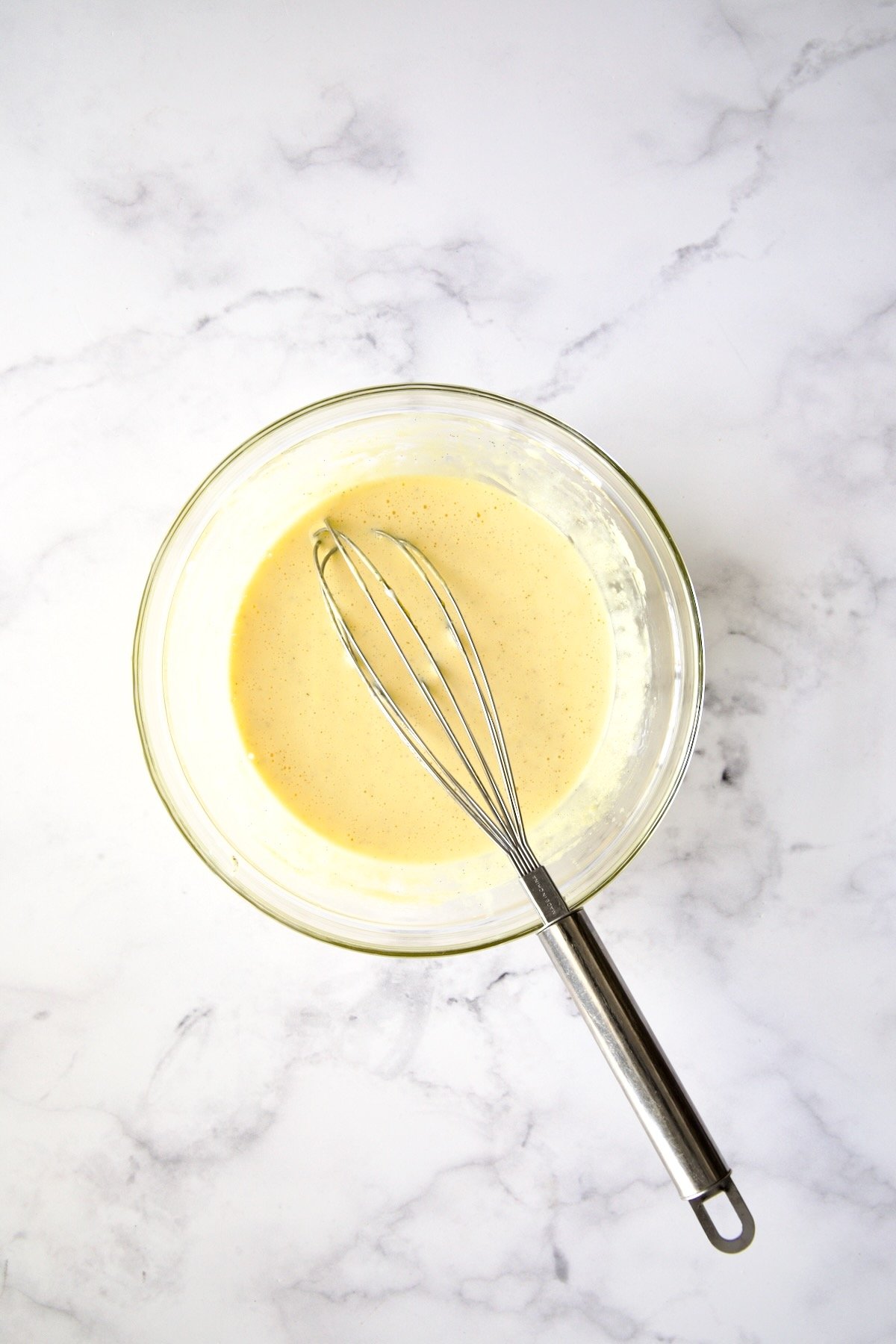 Creme brulee batter with whisk in glass bowl.