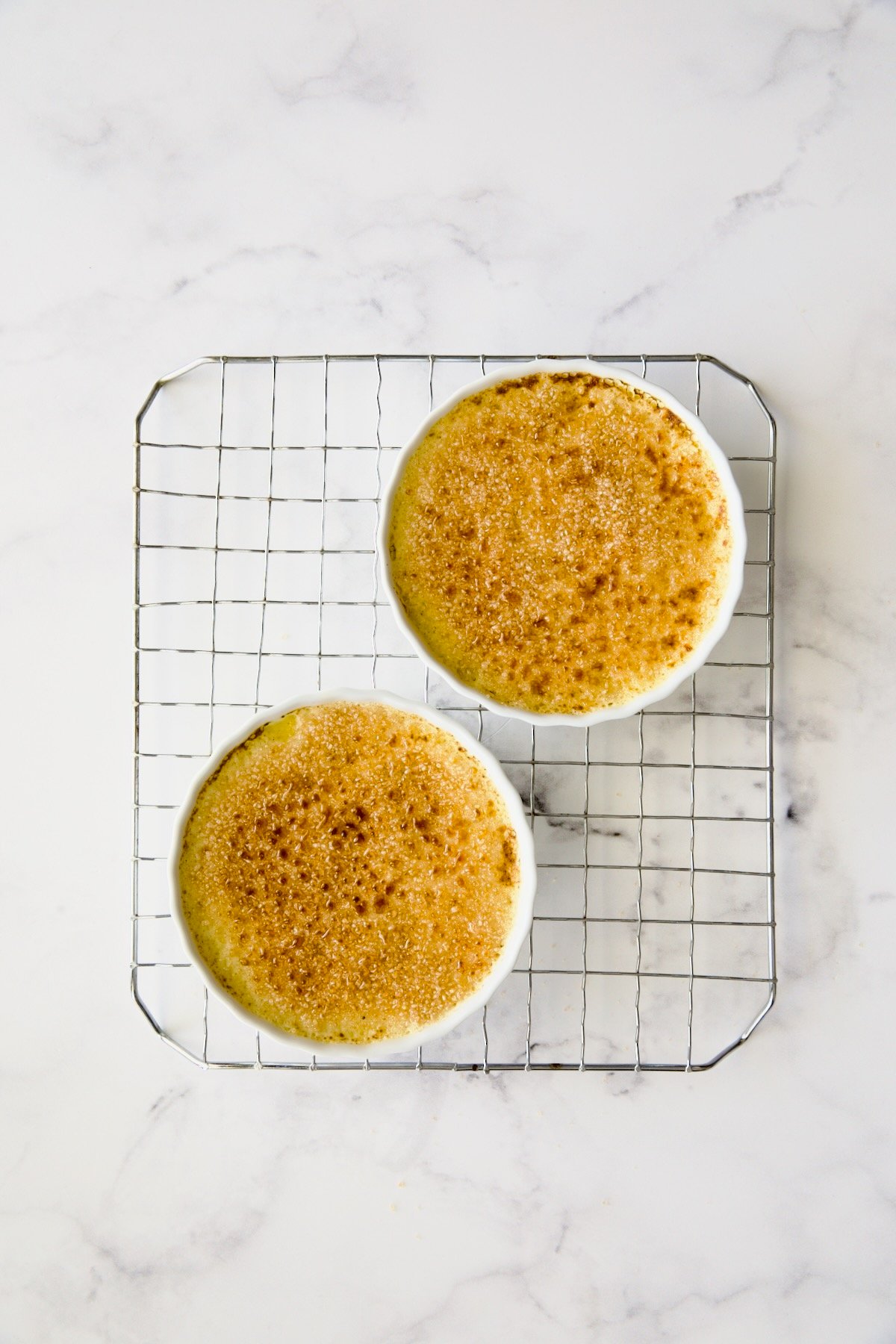 Two completed Classic Creme Brulees with burned sugar on wire rack.
