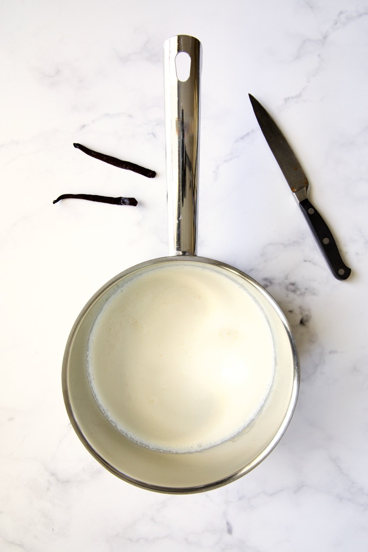 Heavy cream in stainless steel saucepan with vanilla bean cut in half and pairing knife.