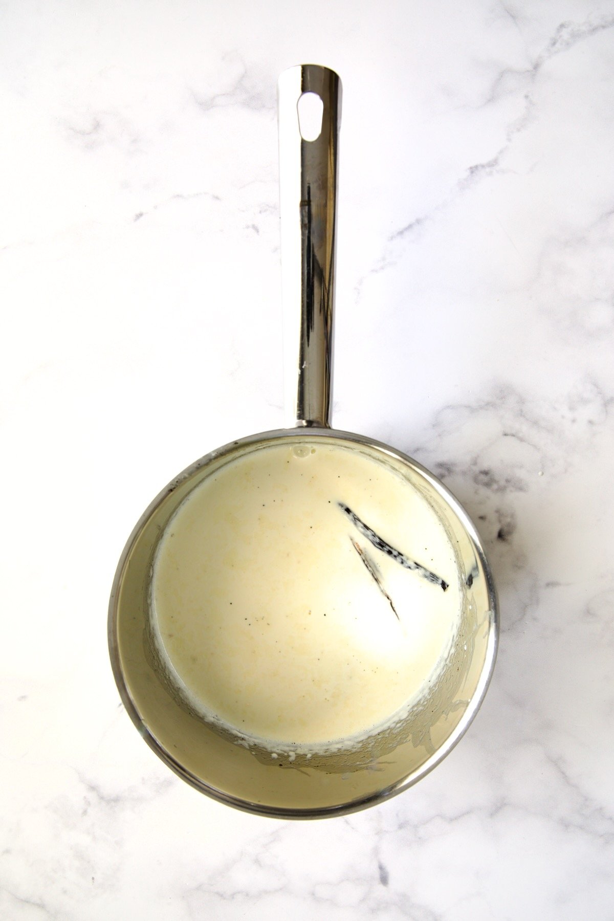 Heavy cream and vanilla bean half in stainless steel saucepan.