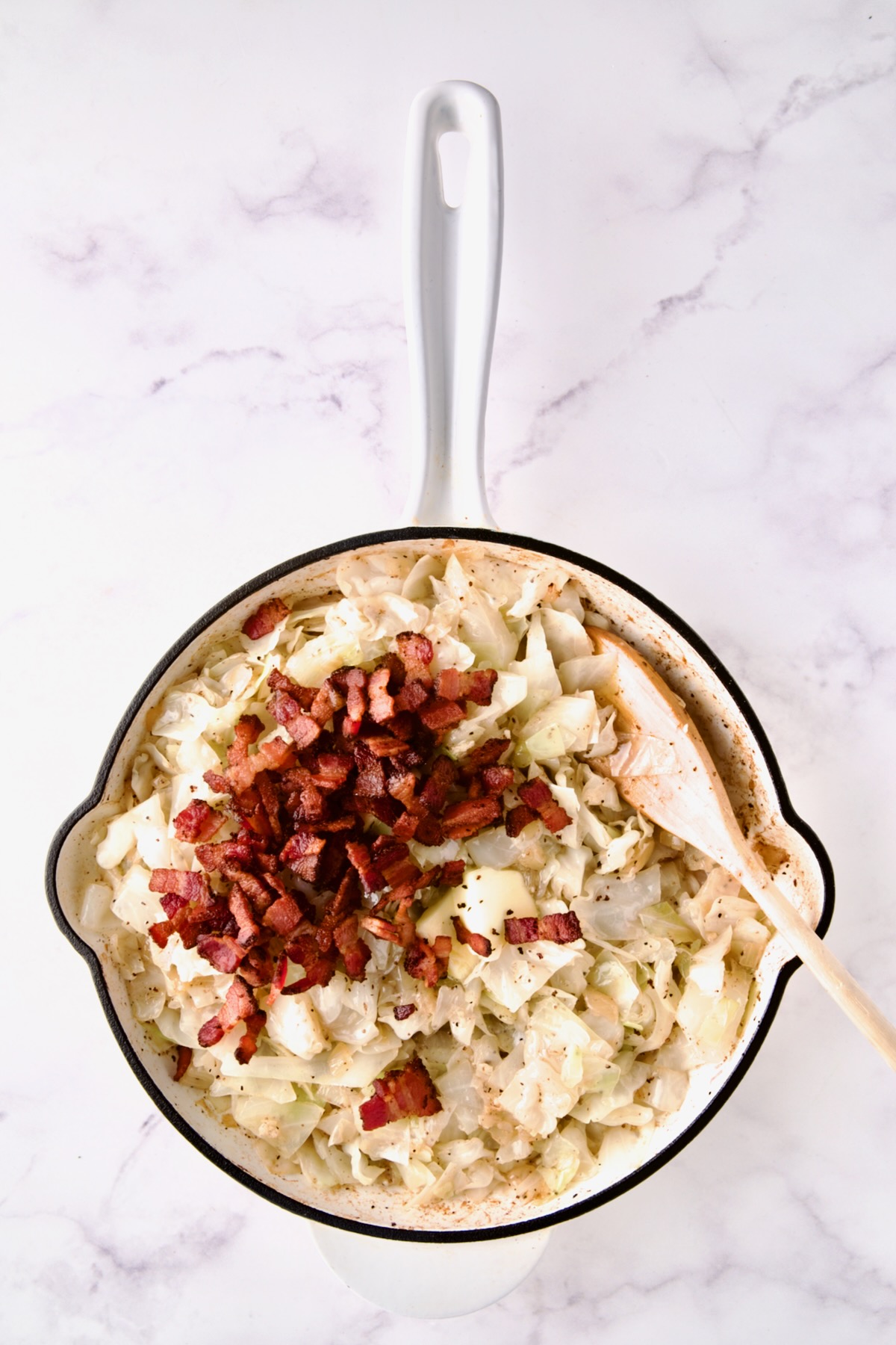 Bacon added back to cooked cabbage in white enamel cast iron skillet.