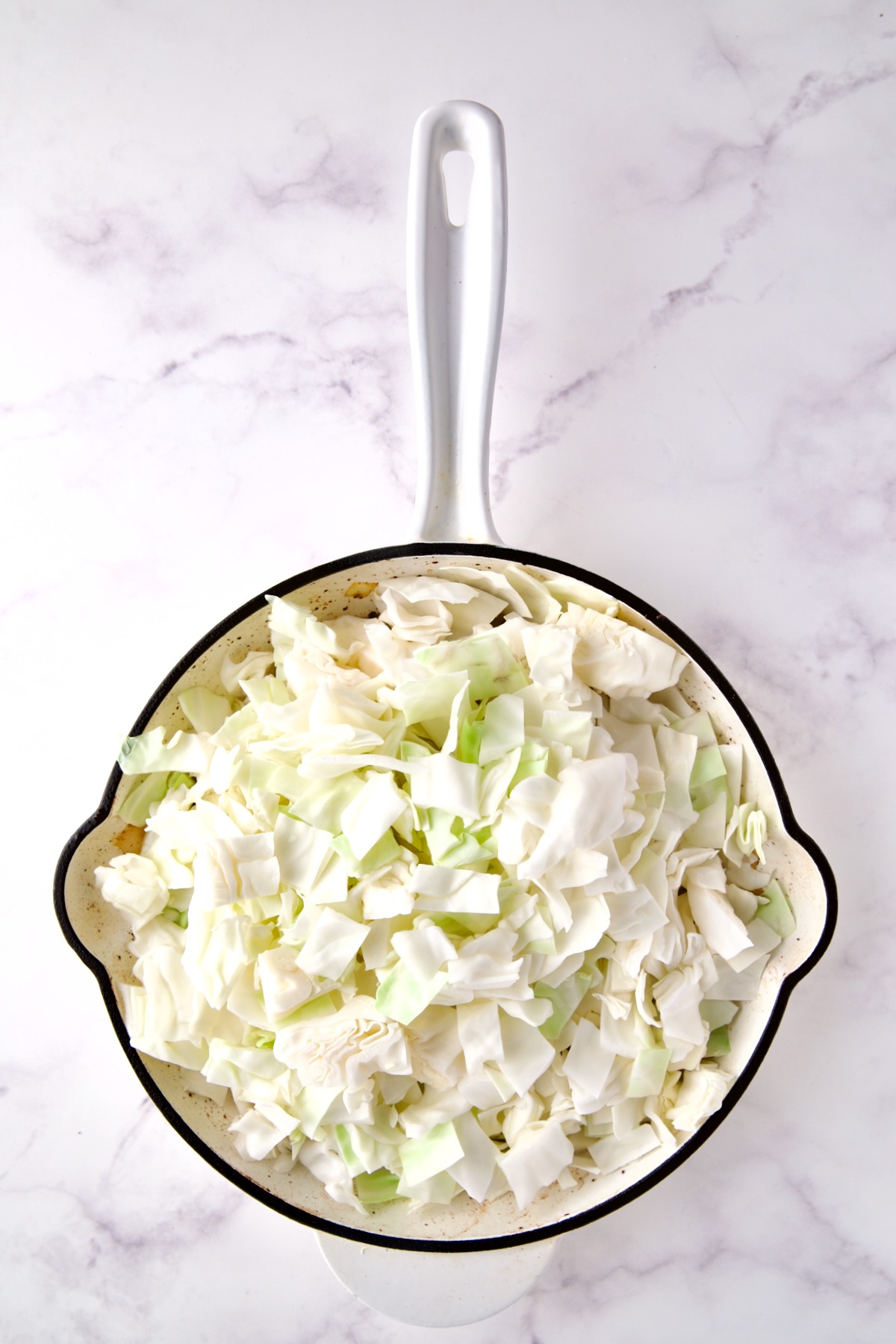 Fresh uncooked cabbage in white enamel cast iron skillet.