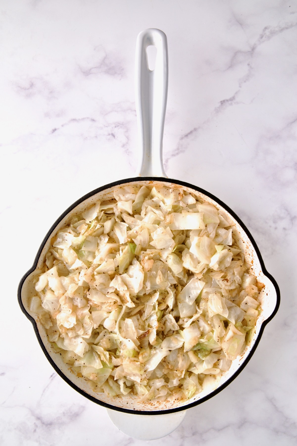 Lightly cooked cabbage in white enamel cast iron skillet.