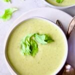 Cream of Celery Leaves Soup in white bowl on white plate with antique spoons.