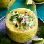 Mango Gazpacho on metal tray garnished with cilantro and lime wedges.