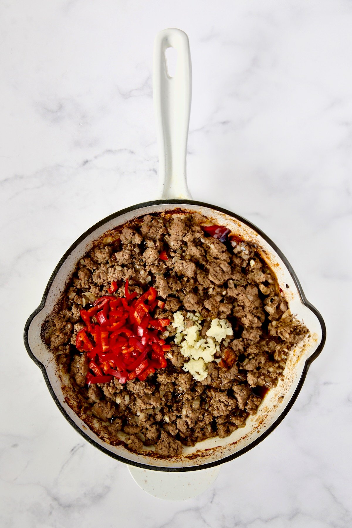 Cooked ground beef in white enamel cast iron skillet with Fresno chiles and garlic added.