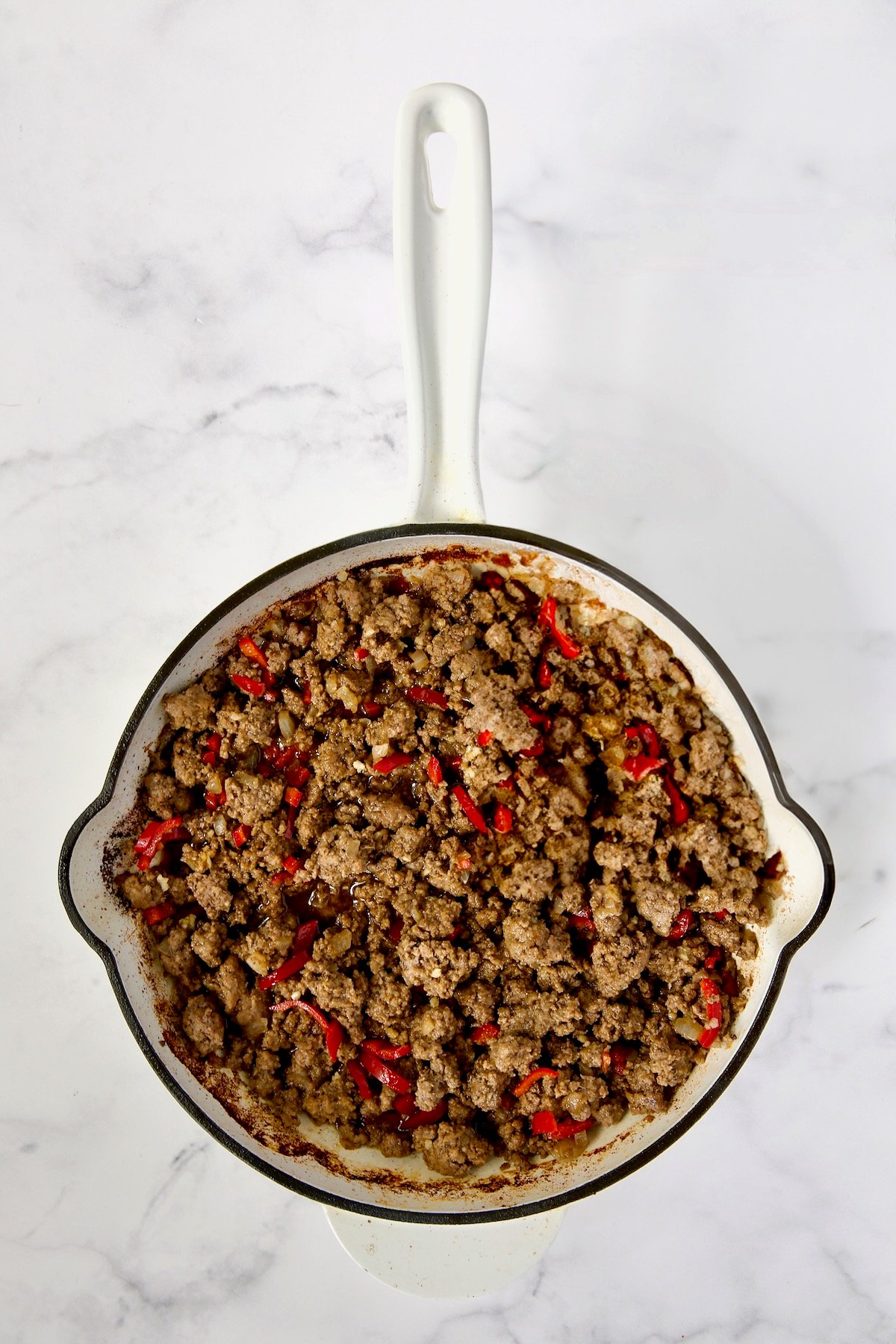 Cooked ground beef and Fresno chiles in white enamel cast iron skillet.