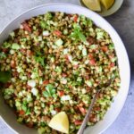 Lentil Tabbouleh in white bowl garnished with fresh mint sprigs and lemon wedges.