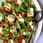 Roasted Cherry Tomato Burrata Caprese Salad on white oval platter with serving utensils.