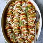 Vegetable Tian in oval baking dish with serving spoon garnished with fresh thyme.