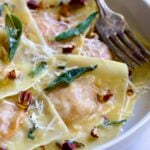 Pumpkin Ravioli with Sage Brown Butter in white pasta bowl garnished with toasted pecans and fried sage leaves.