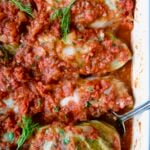 Row of four Polish Stuffed Cabbage in white baking dish with serving fork garnished with fresh dill.
