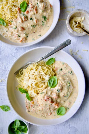Marry Me Chicken in white bowl with angel hair pasta and fork garnished with fresh basil leaves.
