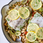 Mediterranean Fish and White Bean Skillet in white cast iron skillet topped with lemon slices.